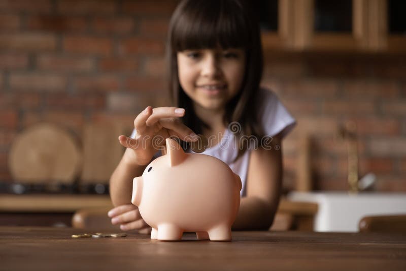 Piccola ispanica che lancia monete a piggybank rosa fotografie stock libere da diritti