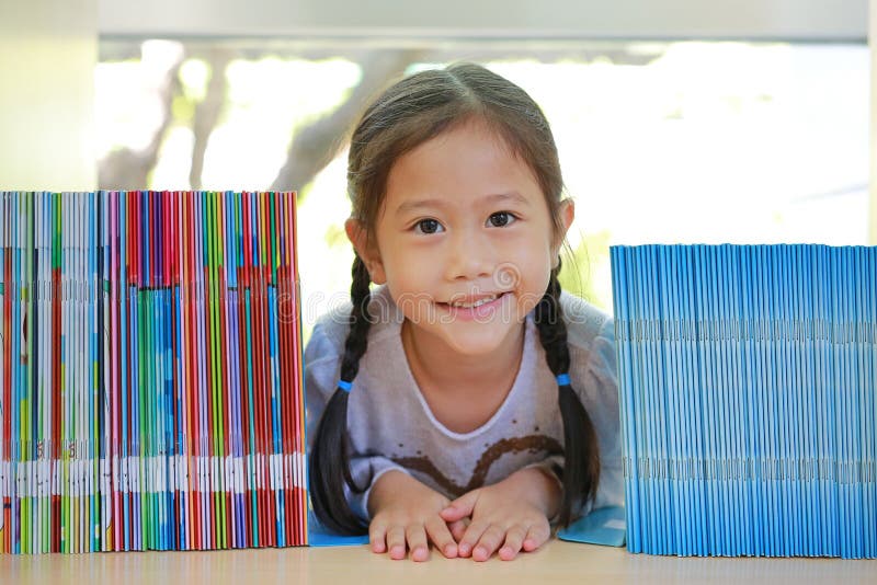 Piccola ragazza asiatica felice del bambino che si trova sullo scaffale per libri alla biblioteca Creatività dei bambini e concet fotografia stock libera da diritti Piccola ragazza asiatica felice del bambino che si trova sullo scaffale per libri alla biblioteca Creatività dei bambini e concet fotografia stock libera da diritti