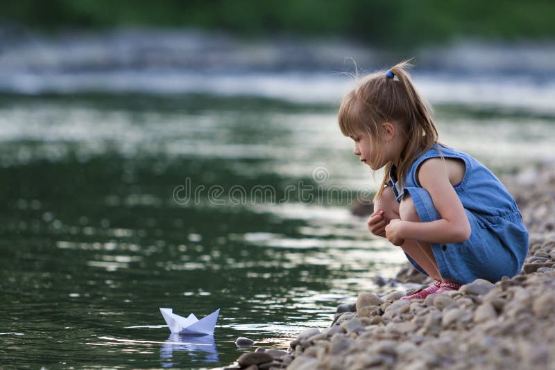 Piccola ragazza bionda sveglia adorabile in vestito blu sul pebbl di riva fotografia stock Piccola ragazza bionda sveglia adorabile in vestito blu sul pebbl di riva fotografia stock