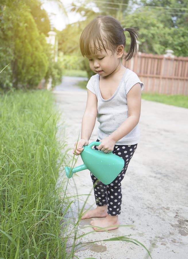 Piccole piante di innaffiatura asiatiche della ragazza immagini stock libere da diritti Piccole piante di innaffiatura asiatiche della ragazza immagini stock libere da diritti