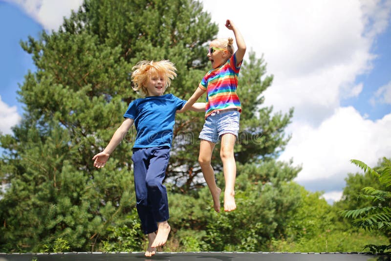 Piccoli bambini carini e felici che saltano sul trampolino fuori il giorno dell'estate fotografia stock