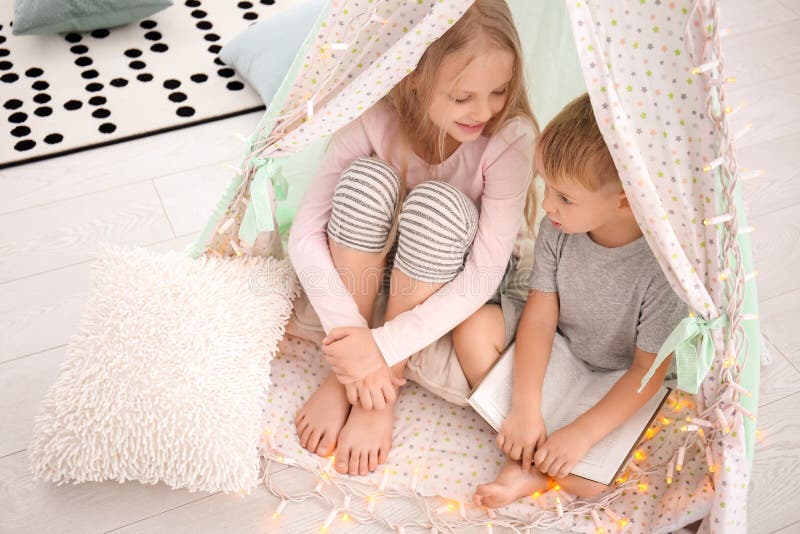 Piccoli bambini svegli con il libro che si siede nel tugurio a casa fotografia stock libera da diritti Piccoli bambini svegli con il libro che si siede nel tugurio a casa fotografia stock libera da diritti