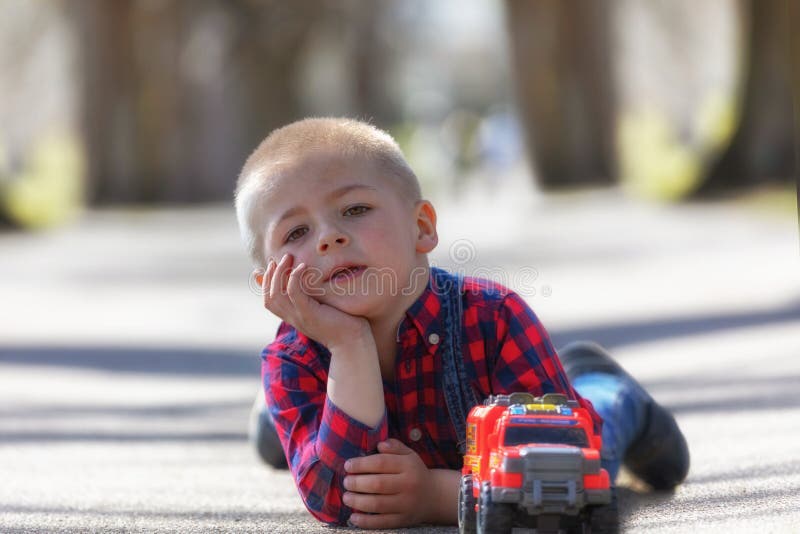 Piccolo bambino sveglio, ragazzo biondo del bambino che gioca all'aperto menzogne alla via fotografia stock libera da diritti Piccolo bambino sveglio, ragazzo biondo del bambino che gioca all'aperto menzogne alla via fotografia stock libera da diritti