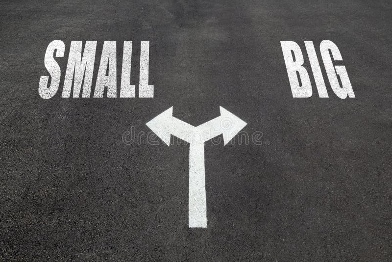 Small vs big choice concept, two direction arrows on asphalt. Small vs big choice concept, two direction arrows on asphalt.