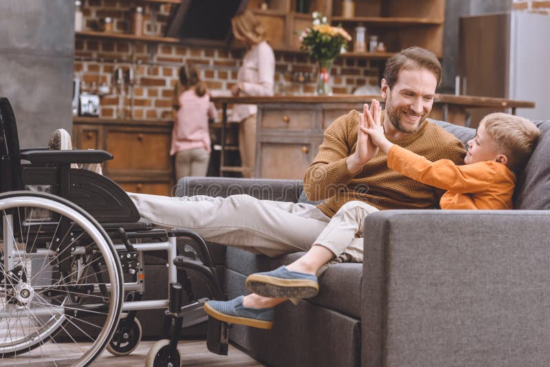 piccolo figlio felice con il padre disabile sorridente che danno su cinque e la condizione della sedia a rotelle illustrazione vettoriale piccolo figlio felice con il padre disabile sorridente che danno su cinque e la condizione della sedia a rotelle illustrazione vettoriale