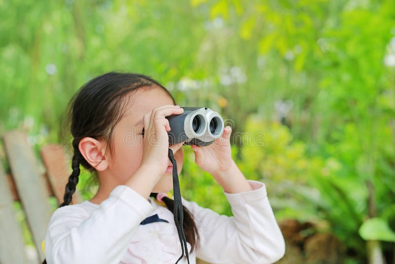 Piccolo ragazza del bambino in un campo che guarda tramite il binocolo in natura all'aperto Esplori ed avventuri il concetto