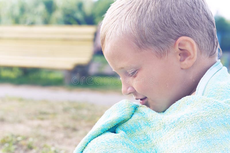 Piccolo ragazzo caucasico che prende il sole dopo la nuotata nel lago Il ragazzo si è coperto di asciugamano e si siede sulla riv immagine stock Piccolo ragazzo caucasico che prende il sole dopo la nuotata nel lago Il ragazzo si è coperto di asciugamano e si siede sulla riv immagine stock
