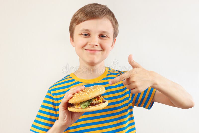 Piccolo ragazzo divertente raccomanda il grande hamburger su fondo bianco fotografia stock libera da diritti Piccolo ragazzo divertente raccomanda il grande hamburger su fondo bianco fotografia stock libera da diritti