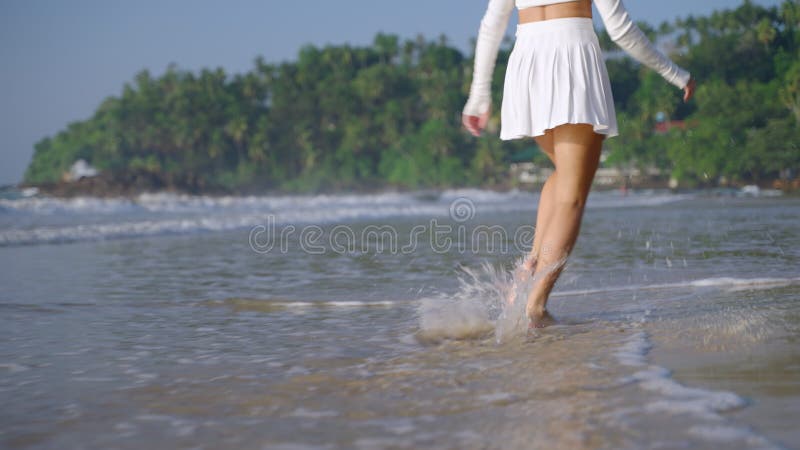 Picioare femele care aleargă și sar în valuri de surf pe mare, făcând stropi de apă. model de mers pe jos de-a lungul mării nisipo stock video