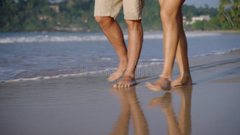 Picioare femele care merg desculț lângă țărmul oceanului. Tineri îndrăgostiți se plimbă pe nisip ud în valuri pe mare stock video footage