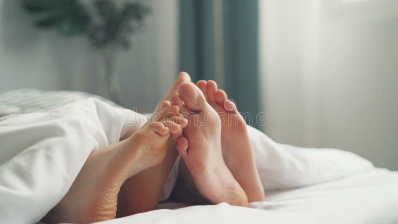 Picioarele masculi și femele atingând sub pătură, două întinse împreună în pat stock footage