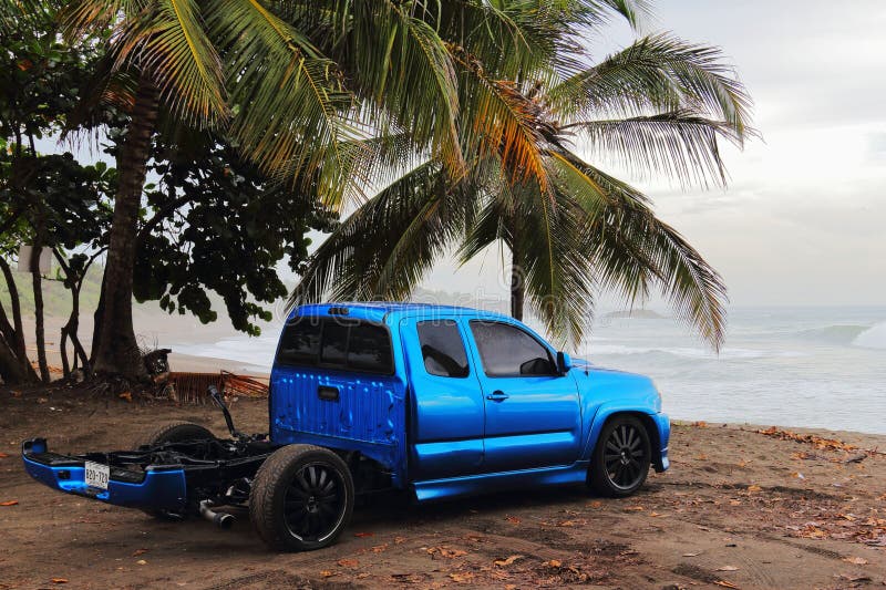 A white pick-up truck with a flatbed parked at a beach with palm trees in the background. A white pick-up truck with a flatbed parked at a beach with palm trees in the background