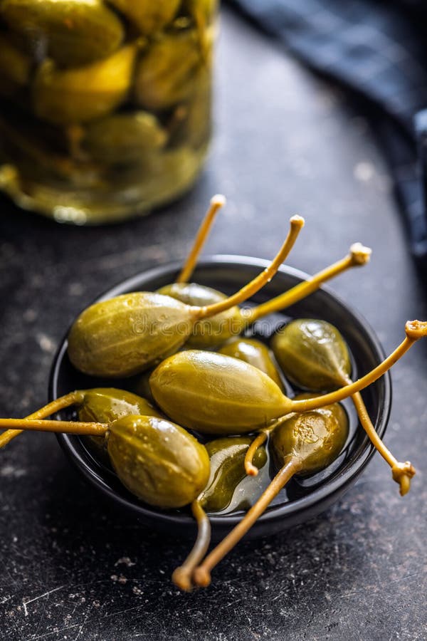 Pickled capers berries in bowl on black table royalty free stock photography