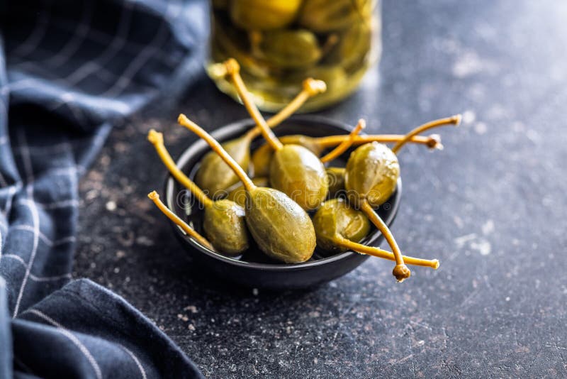 Pickled capers berries in bowl on black table royalty free stock images