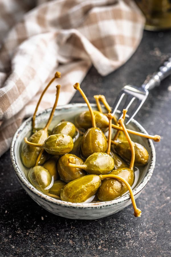 Pickled capers berries in bowl on black table stock photography
