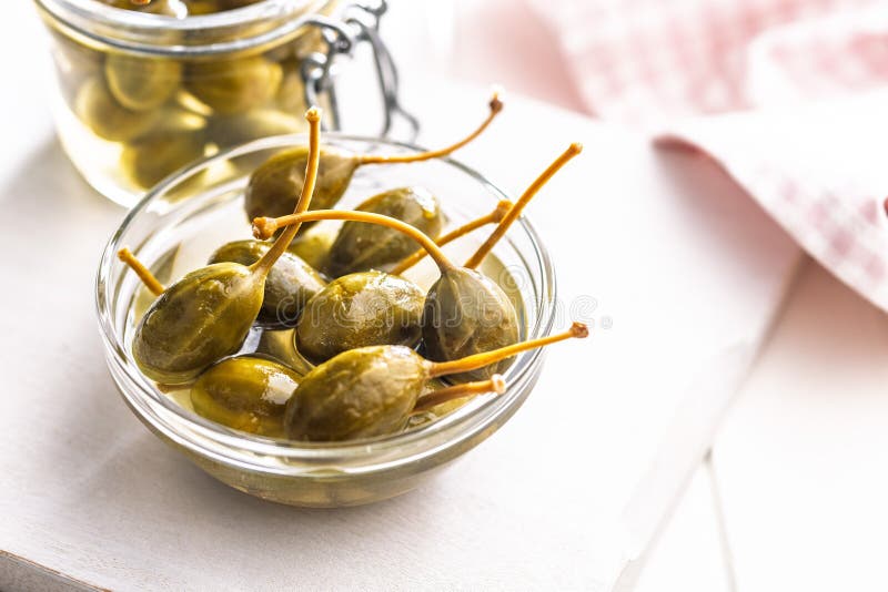 Pickled capers berries in bowl on white table royalty free stock photography