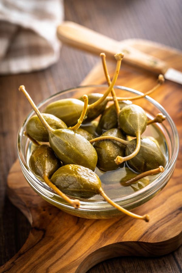 Pickled capers berries in bowl on wooden cutting board royalty free stock photos