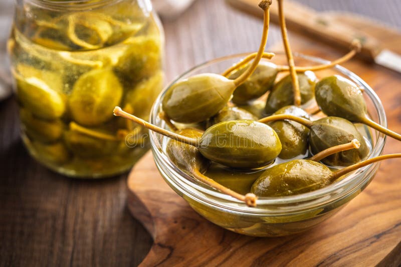 Pickled capers berries in bowl on wooden cutting board royalty free stock images
