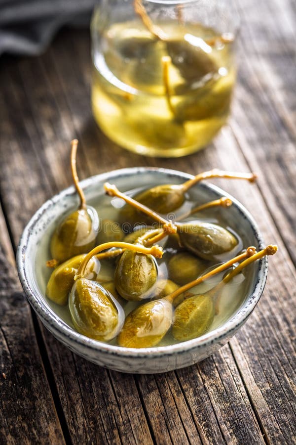 Pickled capers berries in bowl on wooden table stock images