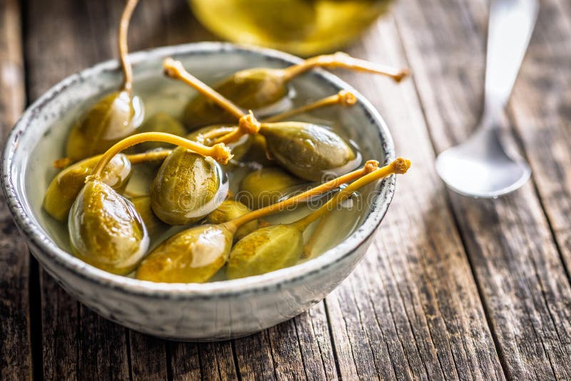 Pickled capers berries in bowl on wooden table royalty free stock photography