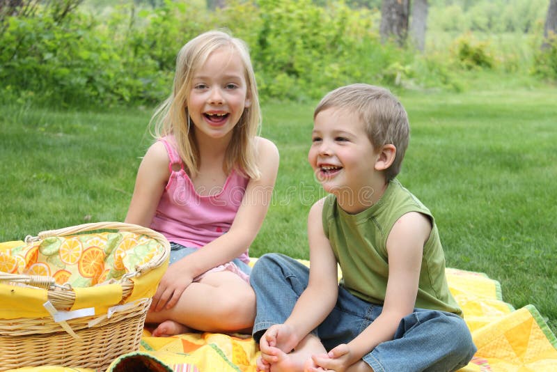 A young brother and sister laughing during a picnic in a grassy meadow.