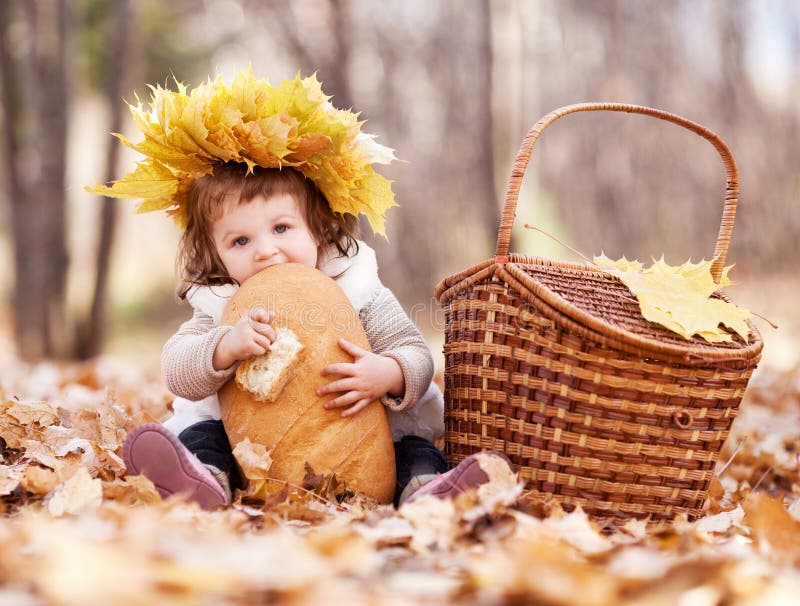 Cute baby girl having a picnic, sitting on the gras in the autumn park and eating a long loaf. Lovely european female stock images, royalty-free photos and pictures