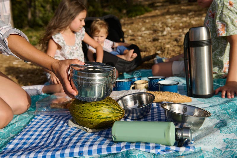 Picnic familiar en la naturaleza con niños disfrutando de comida al aire libre y tiempo de unión. Familia feliz comiendo un picnic en la naturaleza. cierre de alimentos como recipientes de acero inoxidable termo y tazas con niños en el fondo sobre una manta.