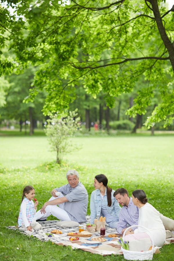 Family of five people sitting on gree lawn, talking and enjoying their picnic in park. Family of five people sitting on gree lawn, talking and enjoying their picnic in park