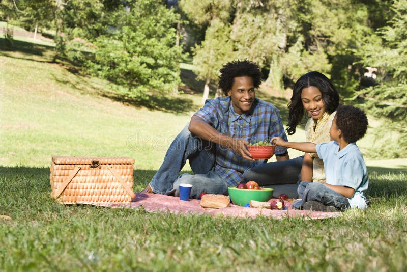 Smiling happy parents and son having picnic in park.