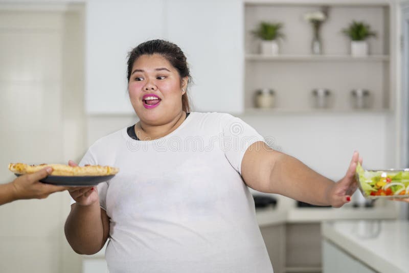 Picture of Asian obese woman eats pizza and rejecting a salad. 