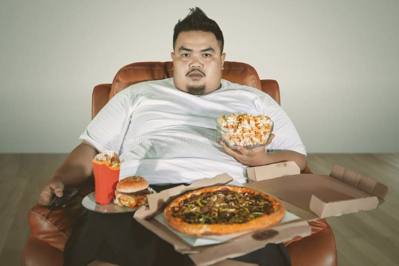 Obese man watching TV with junk foods at home. 