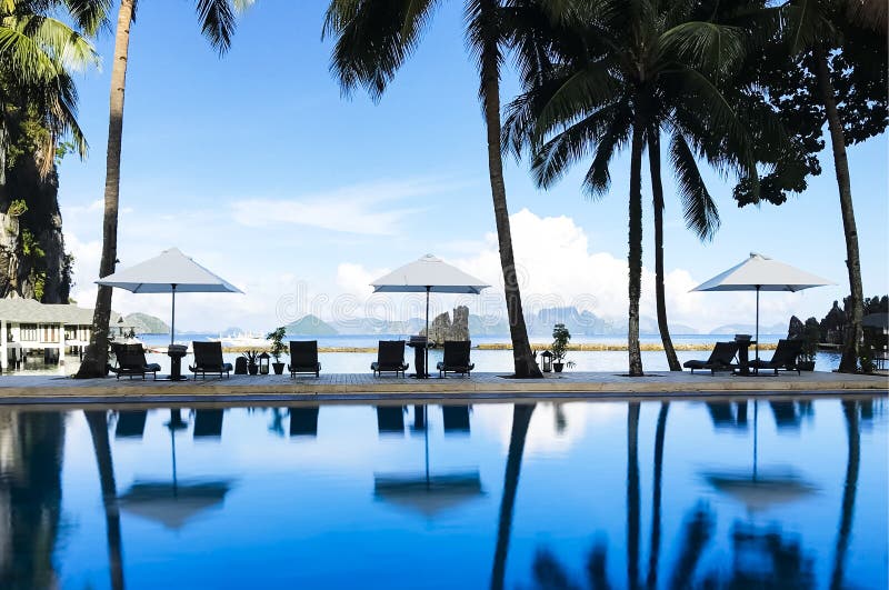 Una foto de nadar piscina Rodeado de acuerdo plegable sillas, blanco paraguas coco árboles, enganar la vista azul el mar montana dónde eso muy relajante sobre el permanecer experiencia.