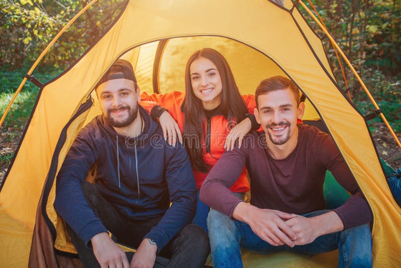 Picture of three young people. Woman sits between men. She holds hands on their shoulders. All of them smile. People are royalty free stock photography Picture of three young people. Woman sits between men. She holds hands on their shoulders. All of them smile. People are royalty free stock photography