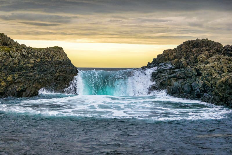 This is a picture of a wave splashing over rocks at the sea at sunset