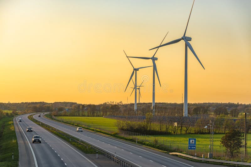 Picture of wind farm generators in the green field close to the road with cars at the sunset