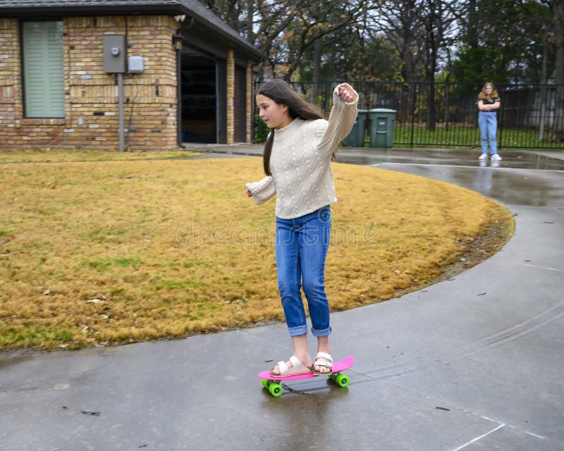 Ten year-old Amerasian girl skateboards down her driveway while her thirteen year old Caucasian cousin watches in Edmond, Oklahoma royalty free stock image Ten year-old Amerasian girl skateboards down her driveway while her thirteen year old Caucasian cousin watches in Edmond, Oklahoma royalty free stock image