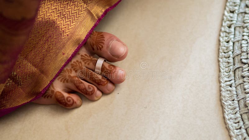 Henna covered south Indian bride's foot with a toe ring. sticking out from below the sari. Henna covered south Indian bride's foot with a toe ring. sticking out from below the sari