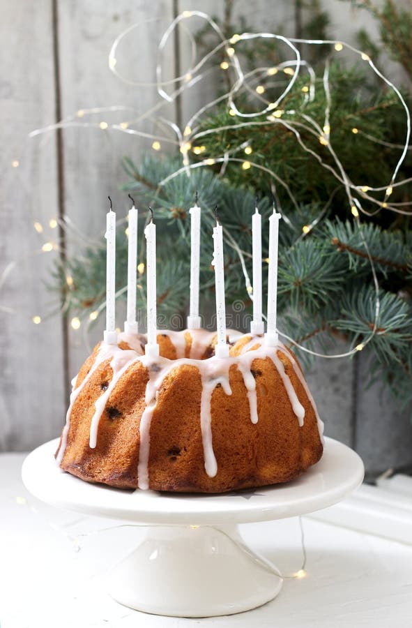 Pie with raisins and icing from powdered sugar on the background of fir branches and garlands. Rustic style.