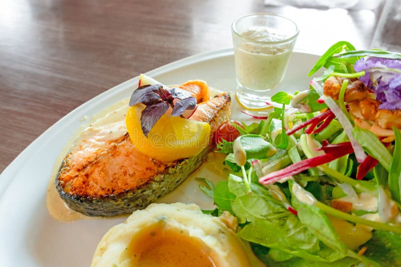 Piec na grillu ?ososiowy stek pokraja? na bielu talerzu z mieszan? jarzynow? sa?atk?, puree ziemniaczane i polew? w szkle, jedzen obraz stock Piec na grillu ?ososiowy stek pokraja? na bielu talerzu z mieszan? jarzynow? sa?atk?, puree ziemniaczane i polew? w szkle, jedzen obraz stock