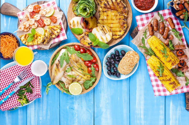 Piec na grillu warzywa, garnela, owoc na, sok i sałatka na błękitnym tle, drewnianym talerzu i kiełbasach, chlebowi obiadowi grul obraz stock Piec na grillu warzywa, garnela, owoc na, sok i sałatka na błękitnym tle, drewnianym talerzu i kiełbasach, chlebowi obiadowi grul obraz stock