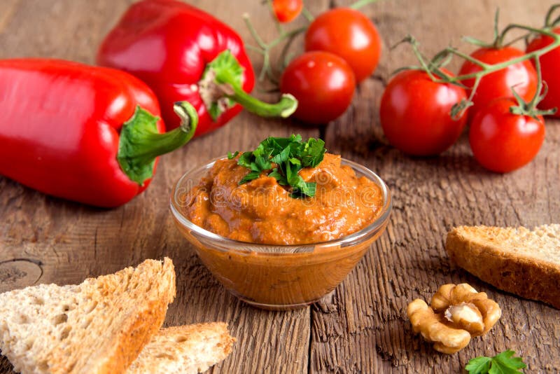 Roasted pepper dip with nuts and bread in glass bowl over rustic wooden background closeup. Roasted pepper dip with nuts and bread in glass bowl over rustic wooden background closeup