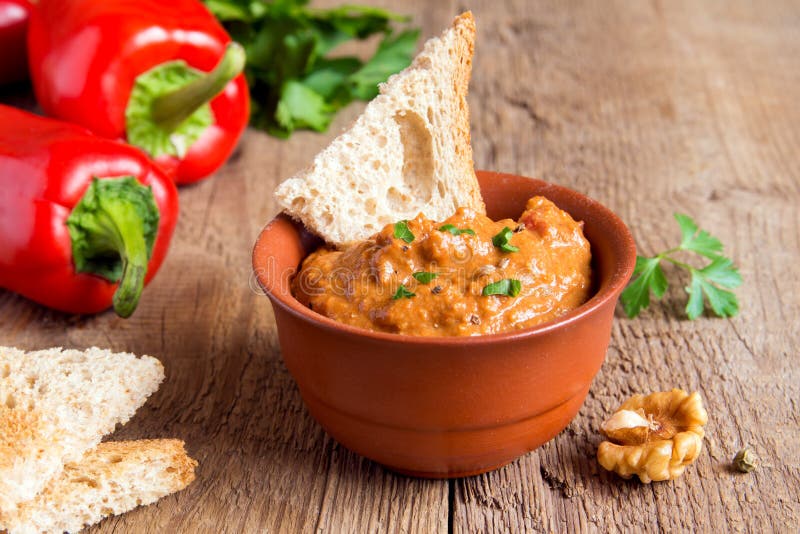 Roasted pepper dip with nuts and bread in ceramic bowl over rustic wooden background closeup. Roasted pepper dip with nuts and bread in ceramic bowl over rustic wooden background closeup