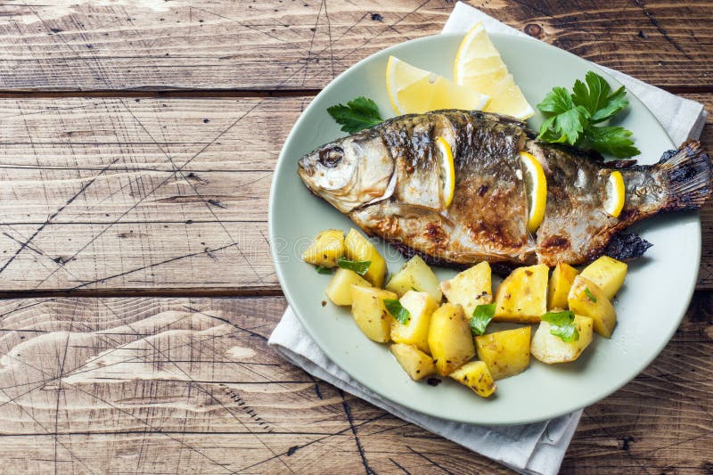 Piec rybi karp z cytryn zieleniami i grule na talerzu Drewniany tło kosmos kopii obrazy stock Piec rybi karp z cytryn zieleniami i grule na talerzu Drewniany tło kosmos kopii obrazy stock