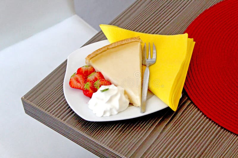 A piece of cheescake with strawberries on a white plate on a wooden table royalty free stock image A piece of cheescake with strawberries on a white plate on a wooden table royalty free stock image