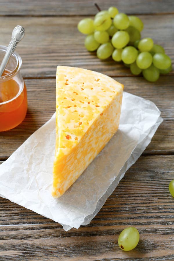 Piece of Cheese with Fresh Grapes and Honey on a Wooden Board Stock