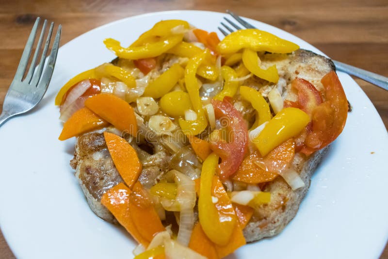 A Piece of Fried Fish with Peppers, Tomatoes and Onions on a Plate with
