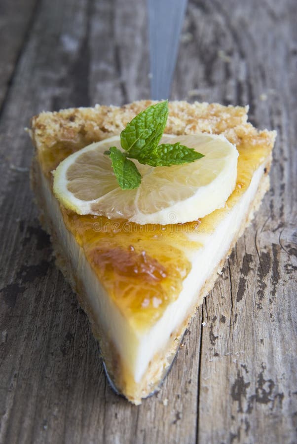 A piece of sweet homemade citrus or lemon tart. Close up piece of pie or cake with mint leaf over rustoc background. Dessert or br