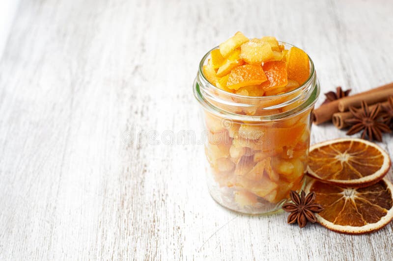 Pieces of homemade candied orange peel coated in sugar in glass jar. Close up view with copy space on a white wooden background. Ingredient for traditional Christmas treats. Pieces of homemade candied orange peel coated in sugar in glass jar. Close up view with copy space on a white wooden background. Ingredient for traditional Christmas treats