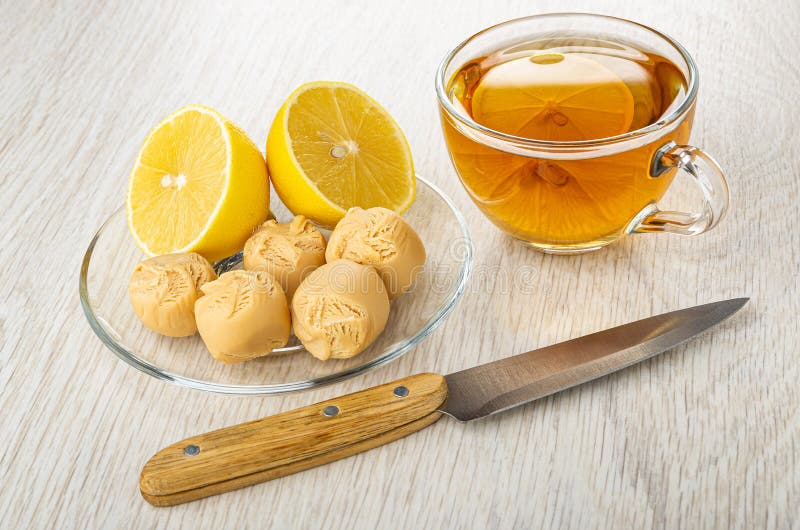 Pieces of lemon, creamy fudge in saucer, cup with tea, knife on wooden table