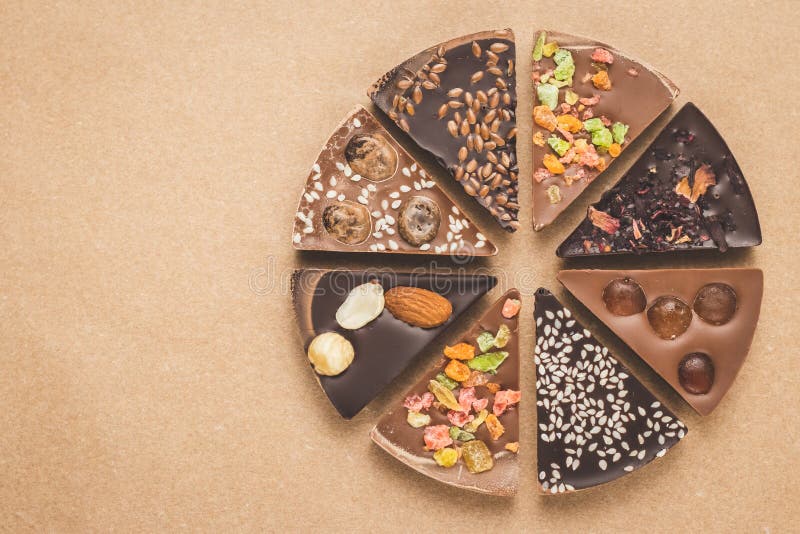 Pieces of milk and dark chocolate with spices on brown background. Slices of chocolates on craft paper, top view. Greeting card